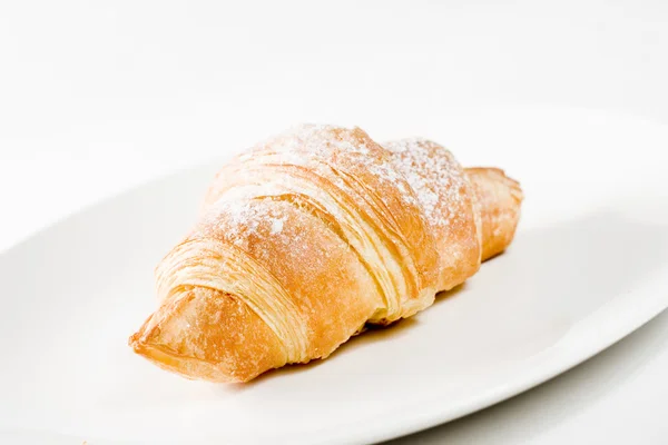 Frisches Croissant auf weißem Teller mit Puderzucker — Stockfoto