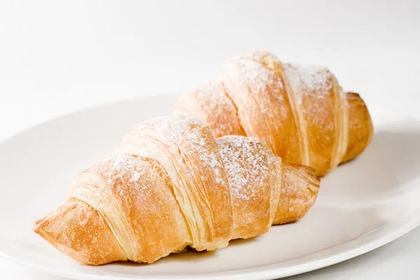 Fresh croissants on white plate with powdered sugar — Stock Photo, Image