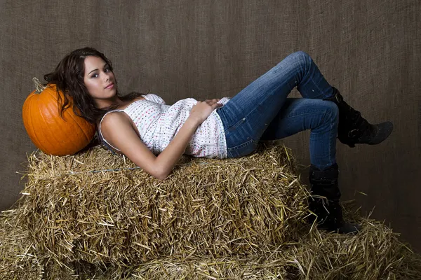 年轻的黑发女孩休息她的头在南瓜上的稻草捆上 — 图库照片