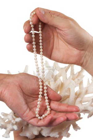 Un collier de perles dans ses mains sur fond de corail 